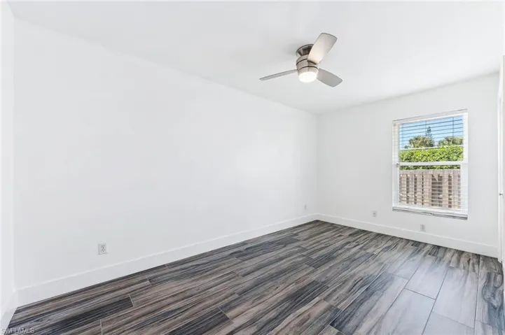 Unfurnished room with dark wood-type flooring, baseboards, and ceiling fan