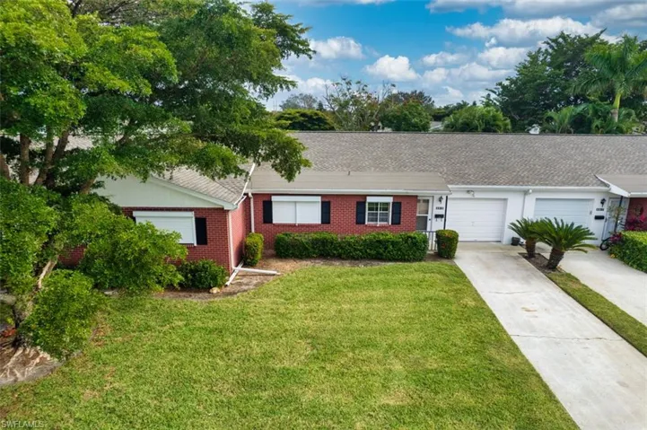 Ranch-style home with concrete driveway, a front lawn, roof with shingles, and brick siding
