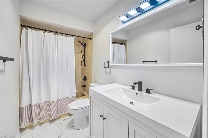Bathroom with shower / tub combo, vanity, and light marble finish floors