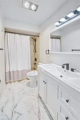 Bathroom with shower / bath combination with curtain, light marble finish flooring, and vanity