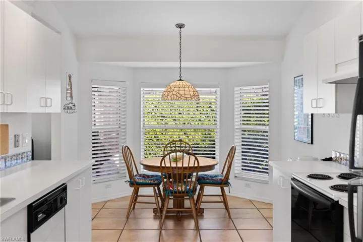 Kitchen with lofted ceiling, white dishwasher, white cabinetry, and hanging light fixtures