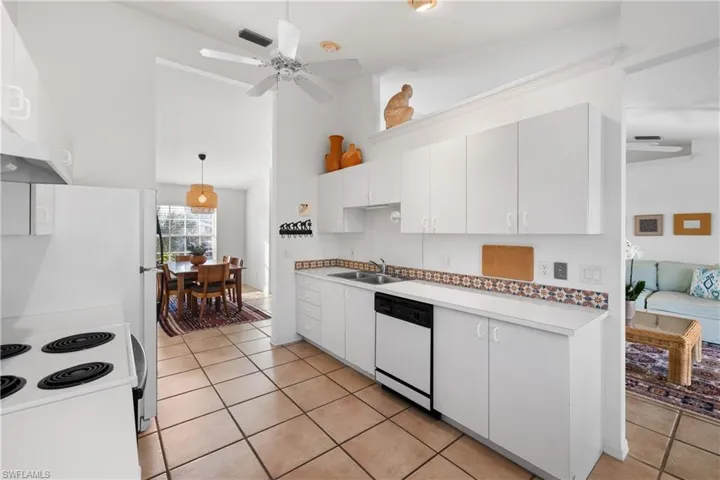 Kitchen featuring white appliances, hanging light fixtures, ceiling fan, sink, and white cabinetry