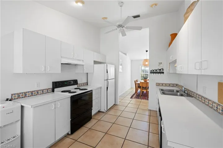 Kitchen with electric range, white refrigerator, white cabinets, and sink