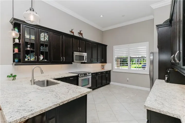 Kitchen with ornamental molding, tasteful backsplash, appliances with stainless steel finishes, light tile patterned flooring, and light stone counters