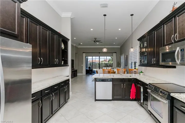 Kitchen with ornamental molding, appliances with stainless steel finishes, light stone countertops, a ceiling fan, and a peninsula