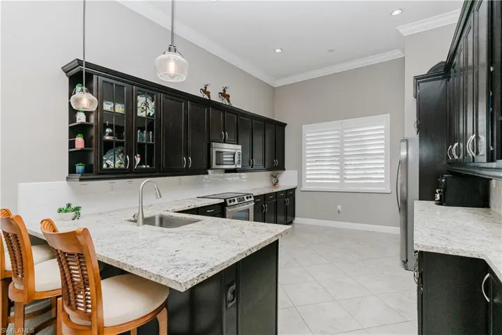 Kitchen with dark cabinetry, backsplash, crown molding, light stone countertops, and a peninsula