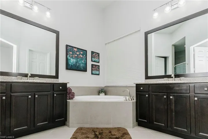 Full bathroom with light tile patterned flooring, two vanities, and a garden tub