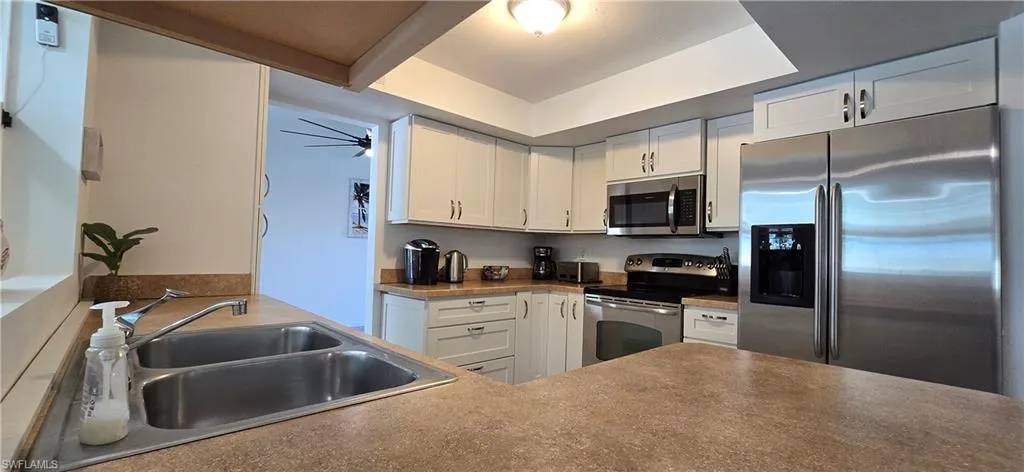 Kitchen featuring appliances with stainless steel finishes, a sink, white cabinets, and dark countertops