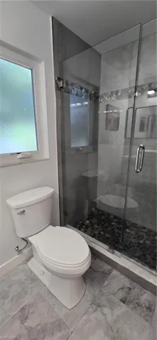 Full bathroom with toilet, a stall shower, and baseboards