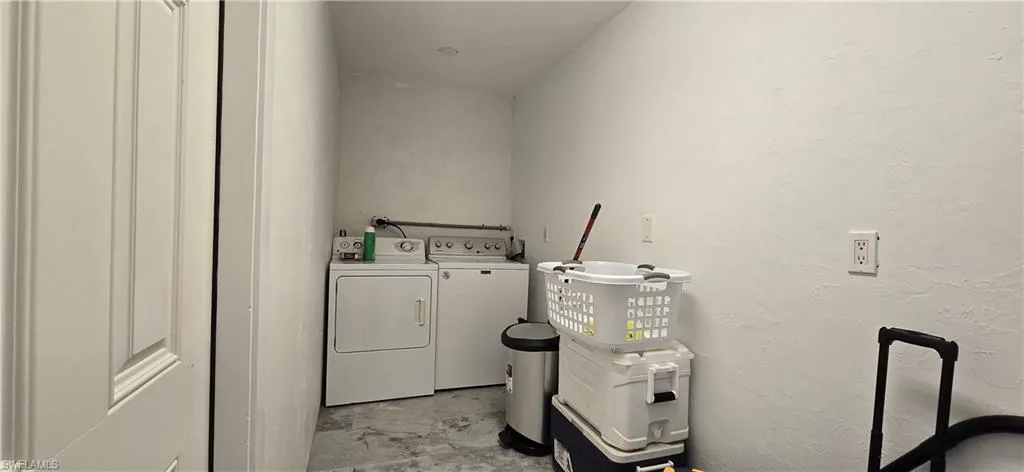 Clothes washing area featuring washing machine and clothes dryer and a textured wall