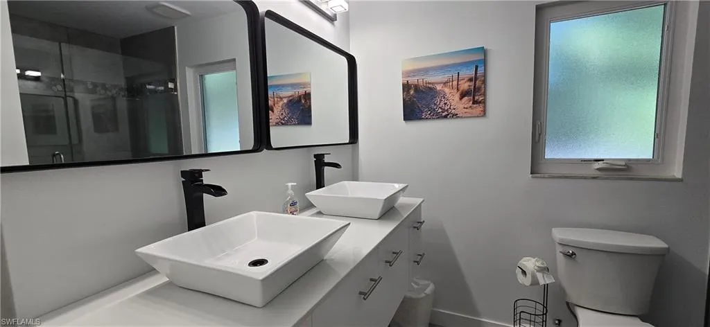 Full bath featuring a stall shower, baseboards, toilet, and double vanity