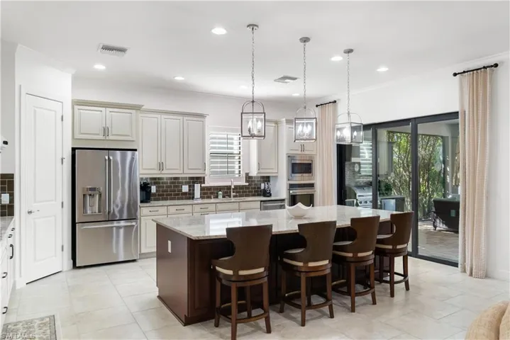 Spacious kitchen featuring an expansive center island, light-toned cabinetry, stainless steel appliances, and large sliding glass doors