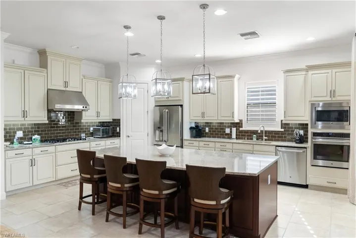 Kitchen featuring a large island, wood cabinetry, built-in stainless steel appliances, a tile backsplash, and overhead pendant lighting