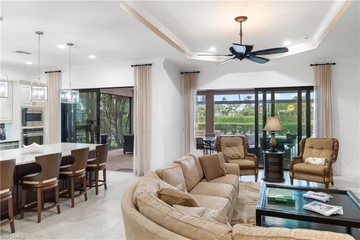 Tray ceiling with a ceiling fan, recessed lighting, expansive sliding glass doors, a large kitchen island with counter seating, and light-toned tile flooring