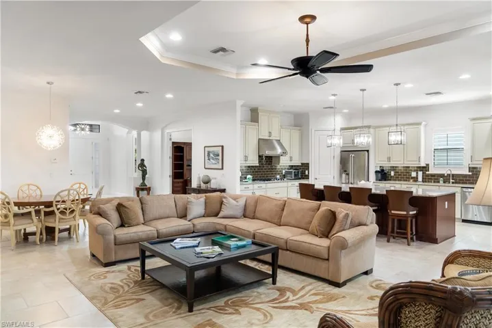 Open-concept living space featuring tray ceilings, recessed lighting, a ceiling fan, and tile flooring