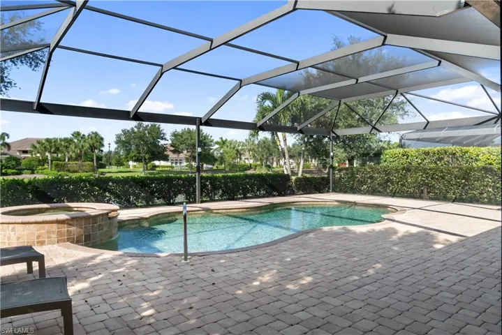 Screened lanai featuring a curved swimming pool, integrated spa with tile surround, and paver patio
