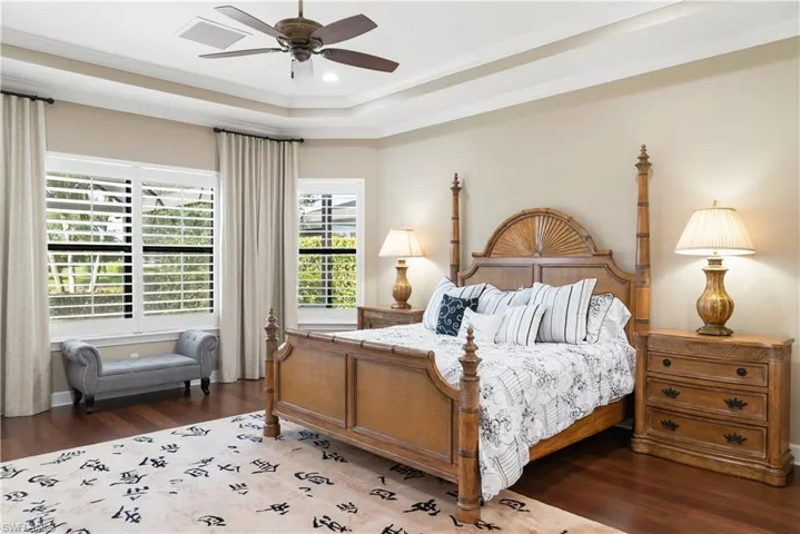 Tray ceiling with a ceiling fan, recessed lighting, wood-finish flooring, and window shutters