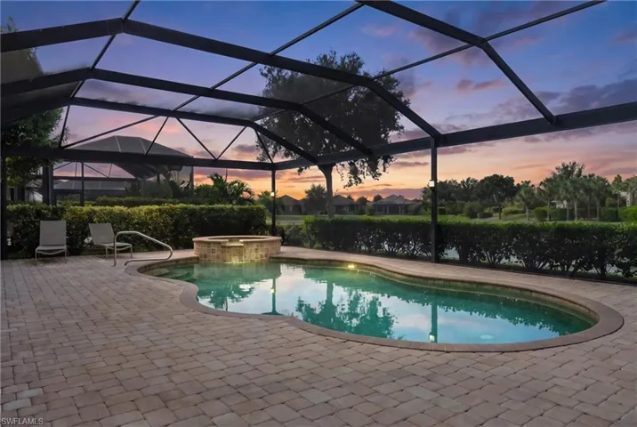 Screened-in outdoor living space featuring a curved swimming pool, integrated spa with stone surround, and paver patio