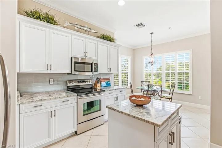 Kitchen with appliances with stainless steel finishes, white cabinetry, light stone countertops, decorative light fixtures, and a kitchen island