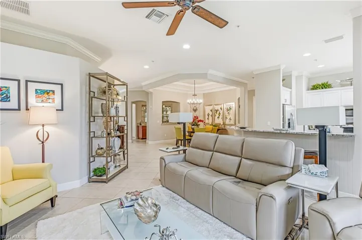 Living room with crown molding, arched walkways, a ceiling fan, light tile patterned flooring, and a chandelier