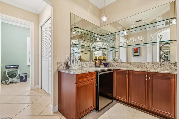 Indoor wet bar featuring crown molding, light tile patterned floors, light stone countertops, hanging light fixtures, and dishwasher