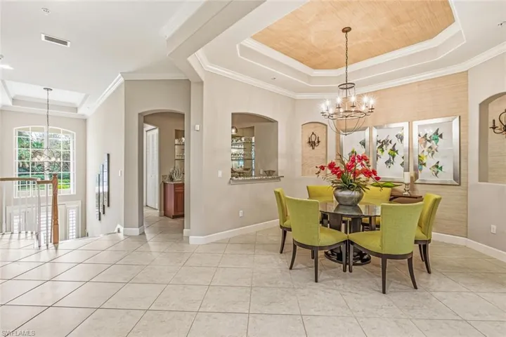 Dining space with a tray ceiling, a chandelier, arched walkways, ornamental molding, and light tile patterned floors