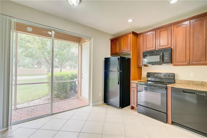 Kitchen featuring black appliances, light tile patterned floors, and light stone counters