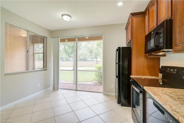 Kitchen featuring light tile patterned floors, light stone counters, and black appliances