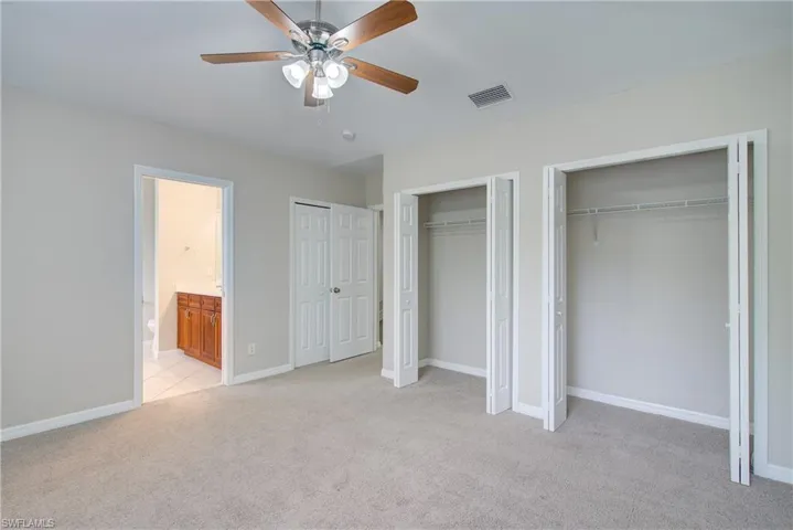 Unfurnished bedroom with ceiling fan, multiple closets, light carpet, and connected bathroom