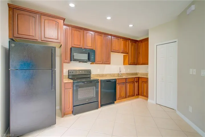 Kitchen featuring black appliances, light tile patterned floors, light stone countertops, and sink