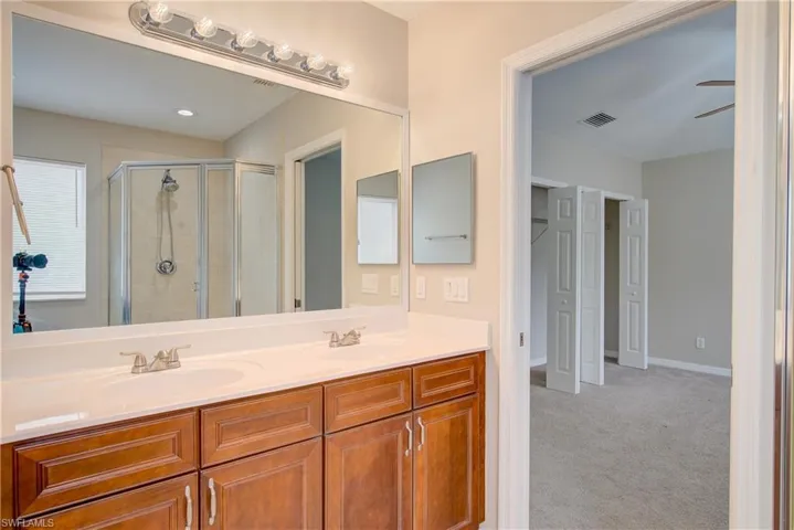 Bathroom featuring ceiling fan, a shower with door, and vanity