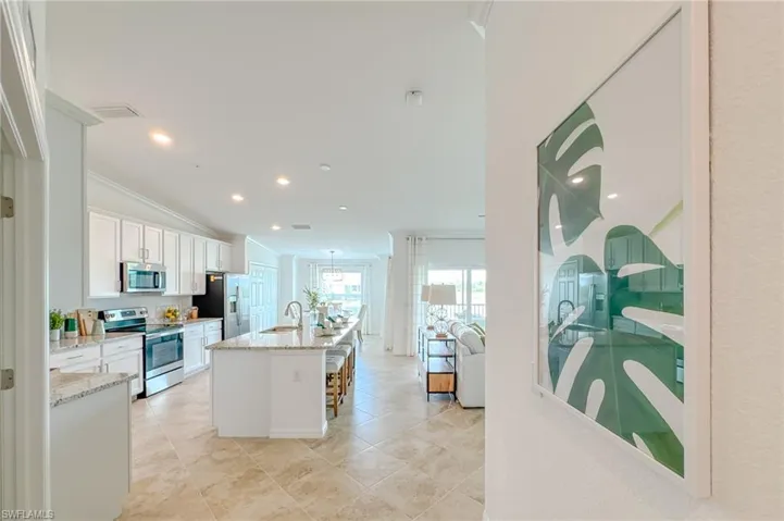 Kitchen with stainless steel appliances, white cabinets, ornamental molding, a kitchen island with sink, and light stone countertops