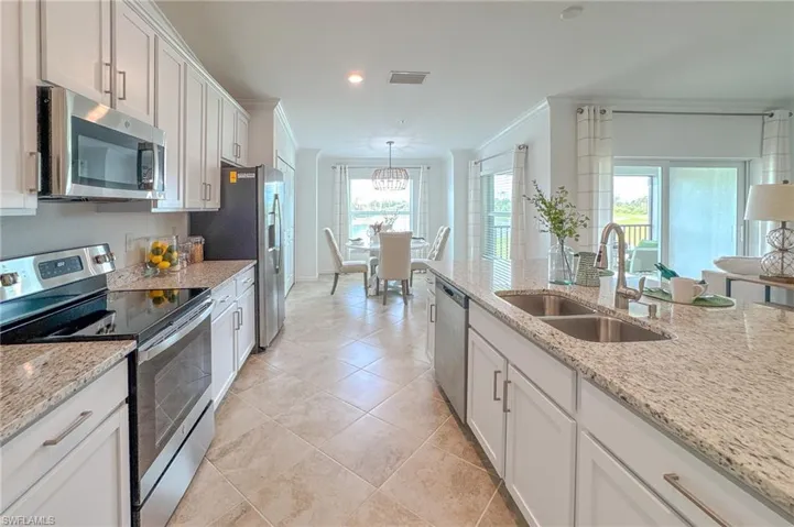 Kitchen featuring appliances with stainless steel finishes, crown molding, white cabinets, light tile patterned flooring, and light stone countertops