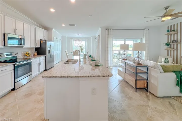 Kitchen with appliances with stainless steel finishes, ornamental molding, white cabinetry, a center island with sink, and light stone counters