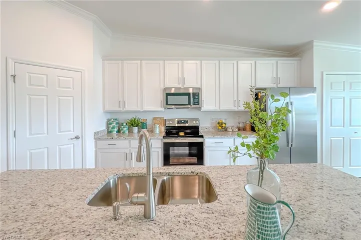 Kitchen featuring ornamental molding, appliances with stainless steel finishes, white cabinetry, light stone countertops, and lofted ceiling