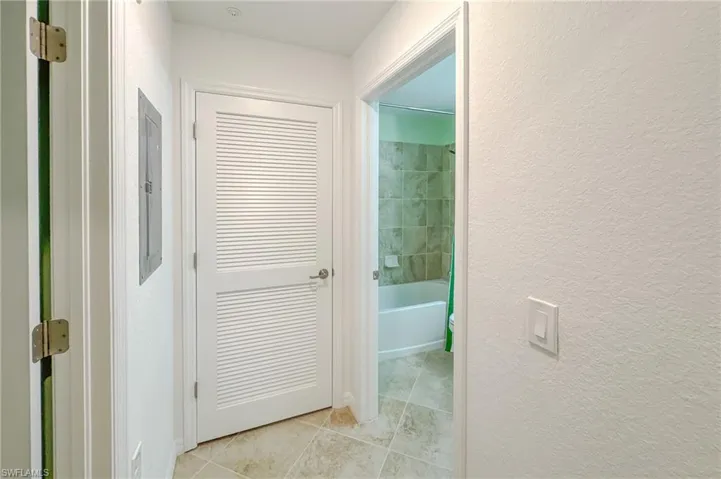 Hall featuring a textured wall, light tile patterned flooring, and electric panel