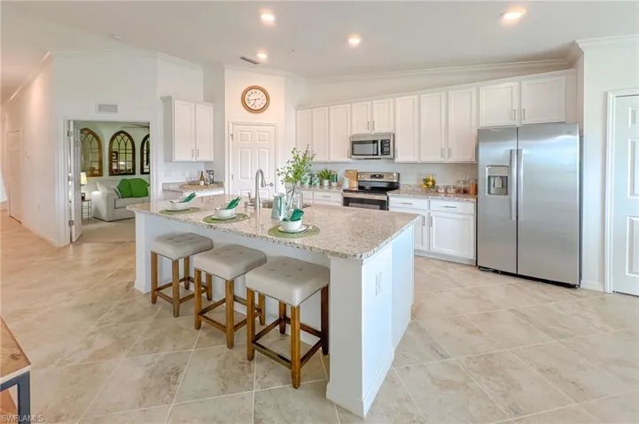 Kitchen featuring stainless steel appliances, ornamental molding, white cabinetry, a center island with sink, and a breakfast bar area