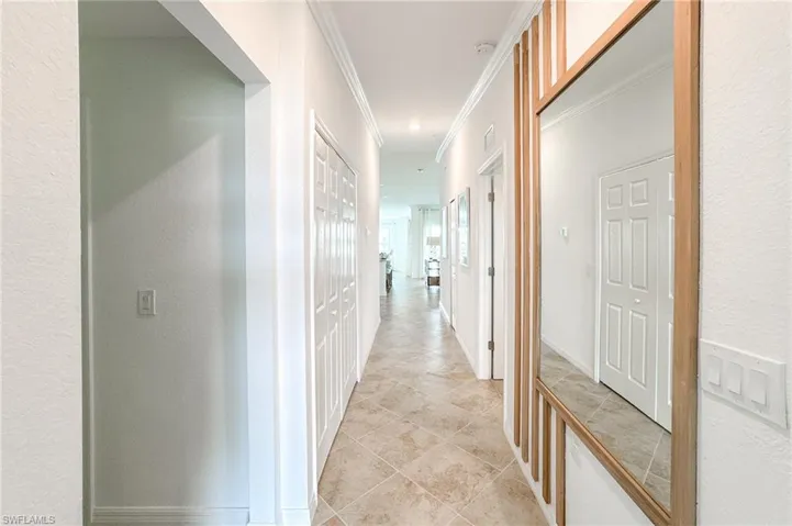 Corridor featuring a textured wall, light tile patterned flooring, and ornamental molding