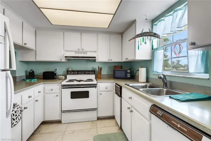 Kitchen with white appliances, white cabinetry, and range hood