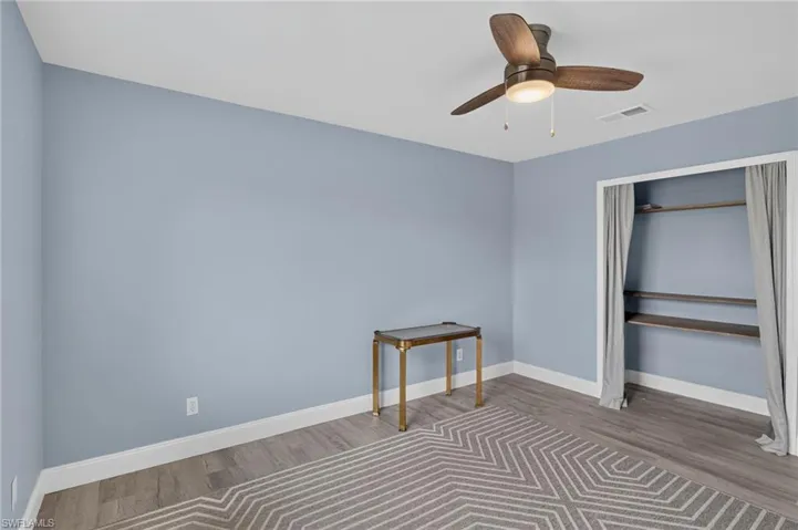 Wood-finish flooring, built-in shelving, white trim, and a ceiling fan with integrated lighting