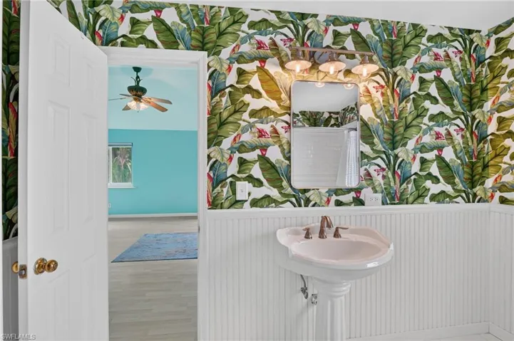 Pedestal sink with a wall-mounted faucet, framed mirror, and a four-light vanity fixture