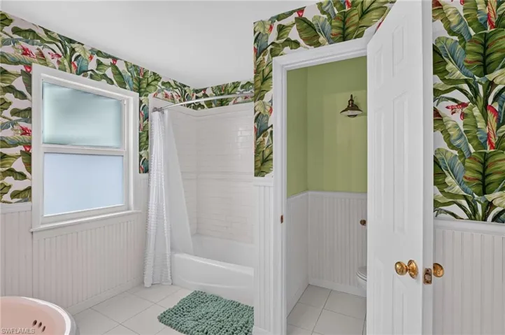 White subway tile shower surround, white paneled wainscoting, and a distinct botanical wallpaper