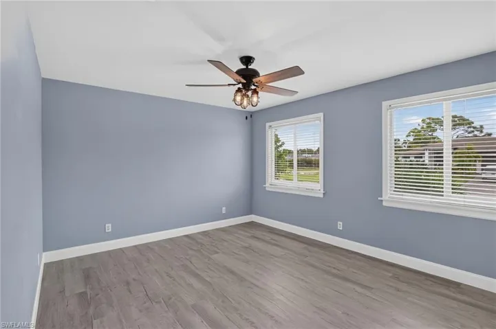 Two large windows with blinds, wood-finish flooring, and a ceiling fan with integrated lighting