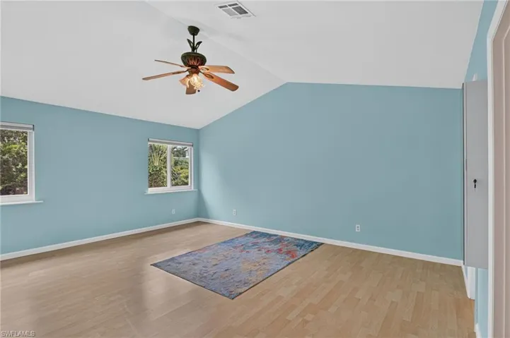 Vaulted ceilings with a ceiling fan, light wood-finish flooring, and two windows