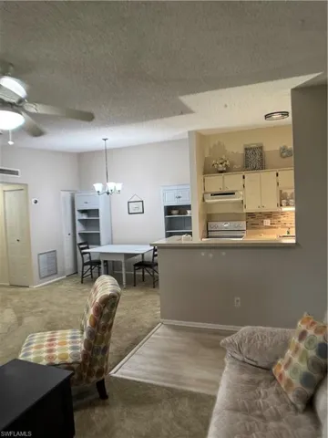 Living area with a textured ceiling, a ceiling fan, a chandelier, and light colored carpet