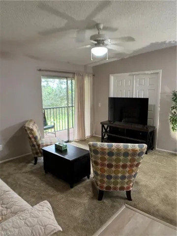 Carpeted living room with a textured ceiling and ceiling fan