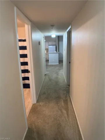 Corridor featuring dark colored carpet and baseboards