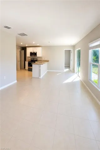Open-concept interior featuring neutral tile flooring, recessed lighting, kitchen cabinetry with stone-finish countertops, and sliding glass doors