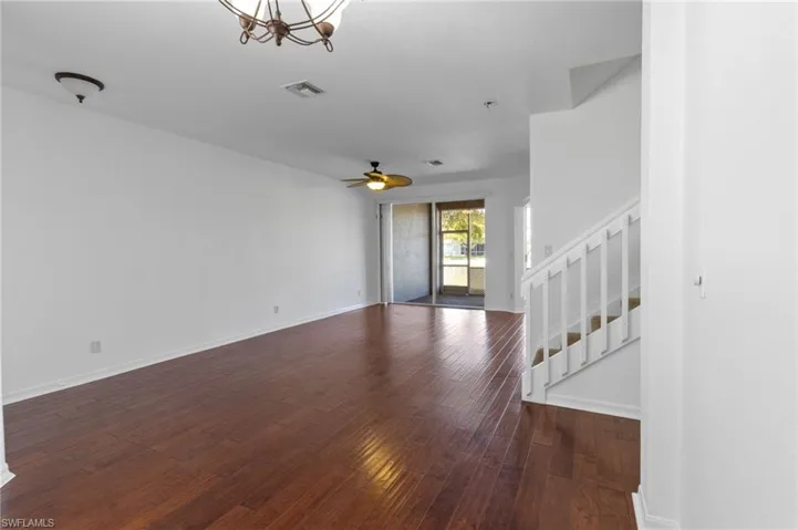 Unfurnished living room with stairs, dark wood-style floors, and ceiling fan