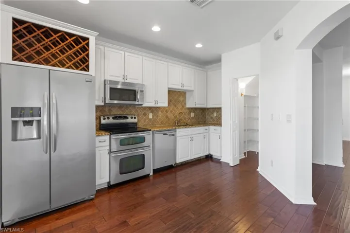 Kitchen with stainless steel appliances, arched walkways, white cabinetry, and recessed lighting